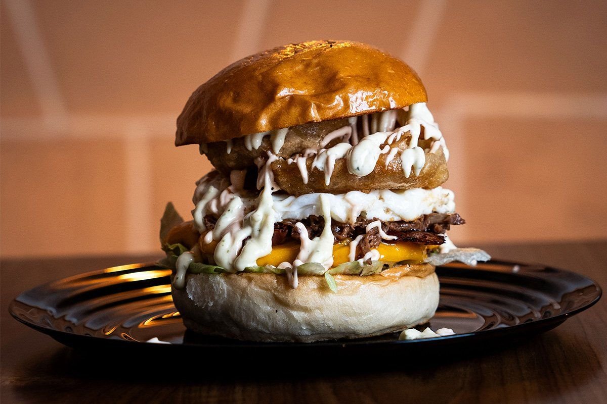 Hamburguesa con aros de cebolla, huevo y salsas, sobre plato negro